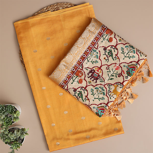A beautiful flat-lay of a vibrant mustard-yellow unstitched Banarasi silk suit fabric, paired with an off-white dupatta featuring intricate, multicolored Kalamkari-style floral and animal motifs.