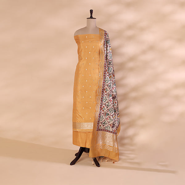 A mannequin displaying a vibrant mustard-yellow unstitched Banarasi silk suit, featuring delicate gold detailing and a contrasting off-white dupatta with intricate floral Kalamkari-style motifs.
