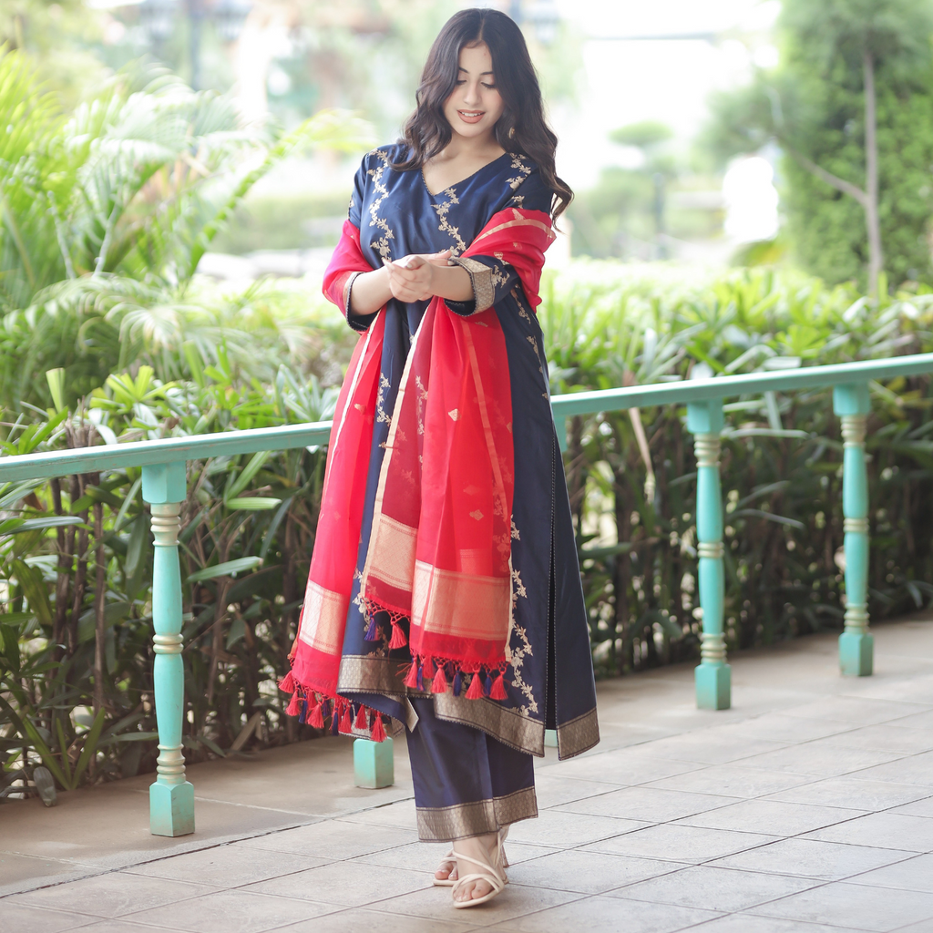 Model in a Navy Blue Handwoven Banarasi Silk Suit with gold zari borders and a contrast Red Kora Silk dupatta in an outdoor setting.