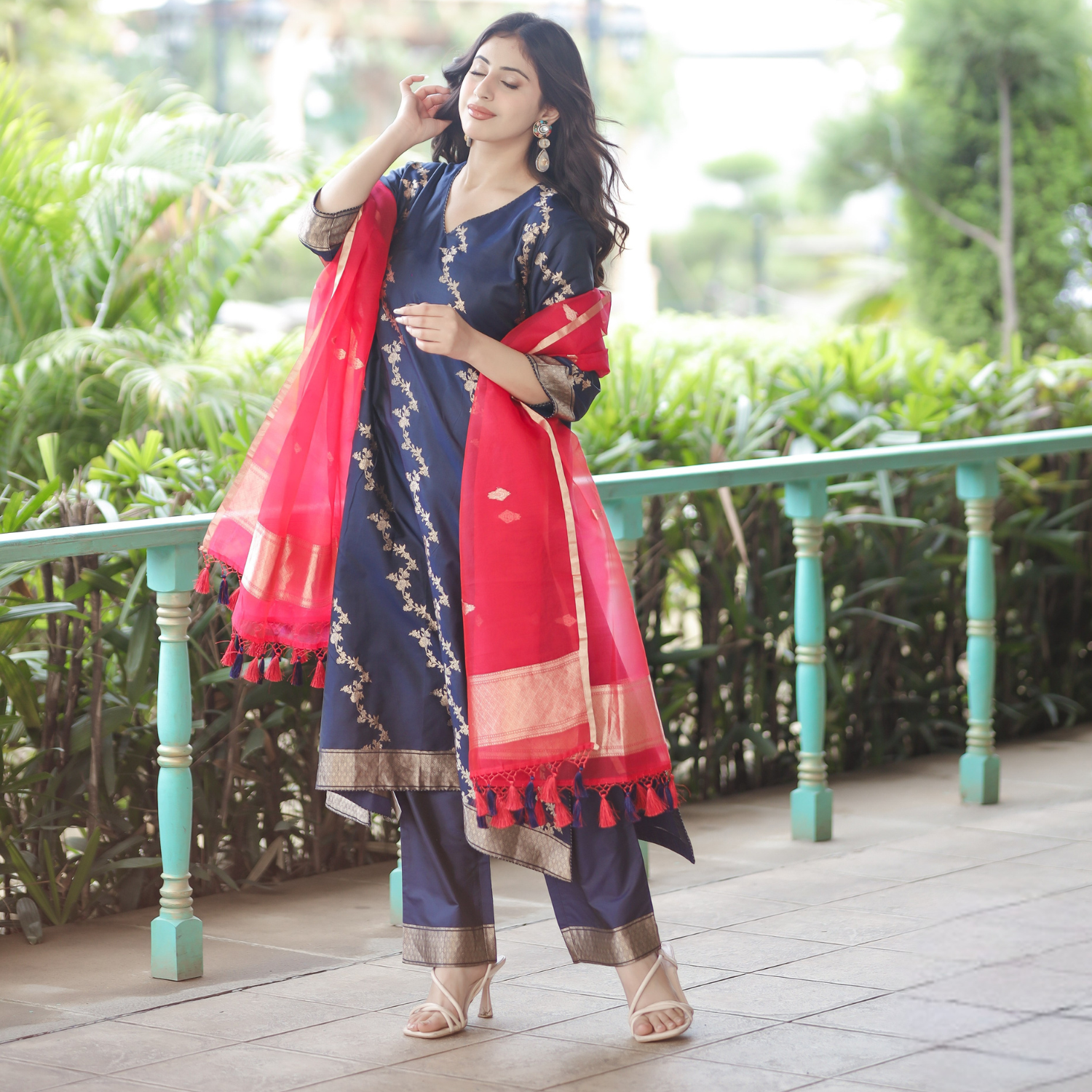 Full-length outdoor pose of a Navy Blue Handwoven Banarasi Silk Suit with gold zari work and a Red Kora Silk Dupatta featuring tassels.
