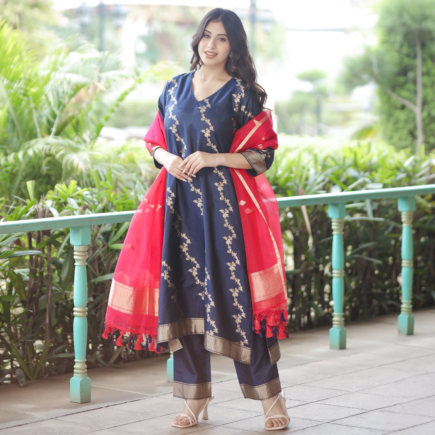 A model posing in a Navy Blue Handwoven Banarasi Silk Suit with 3/4 sleeves and a contrast Red Kora Silk dupatta in an outdoor setting.