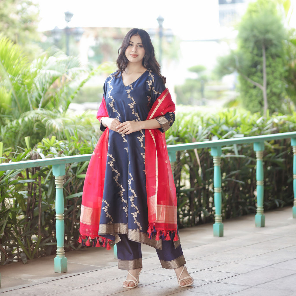 Full-length outdoor view of a Navy Blue Handwoven Banarasi Silk Suit with 3/4 sleeves, gold zari work, and a contrast Red Kora Silk dupatta.