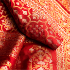 Close-up of the red Nilambari Iktara silk fabric, showcasing the intricate handwoven gold zari motifs and the fine needle-point craftsmanship.