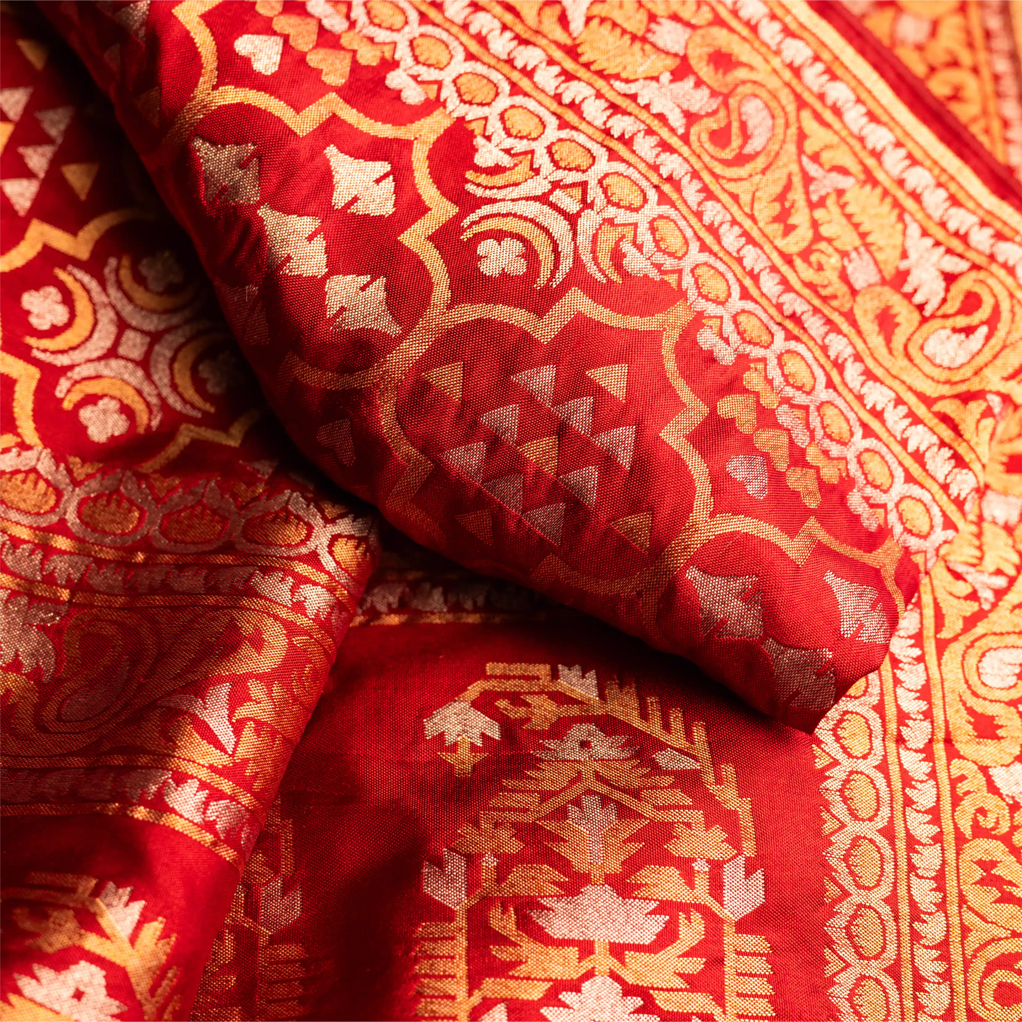 Close-up of the red Nilambari Iktara silk fabric, showcasing the intricate handwoven gold zari motifs and the fine needle-point craftsmanship.