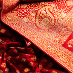 Extreme close-up of the red Nilambari Iktara silk fabric, highlighting a large handwoven gold zari paisley (kalka) motif and the intricate floral border.