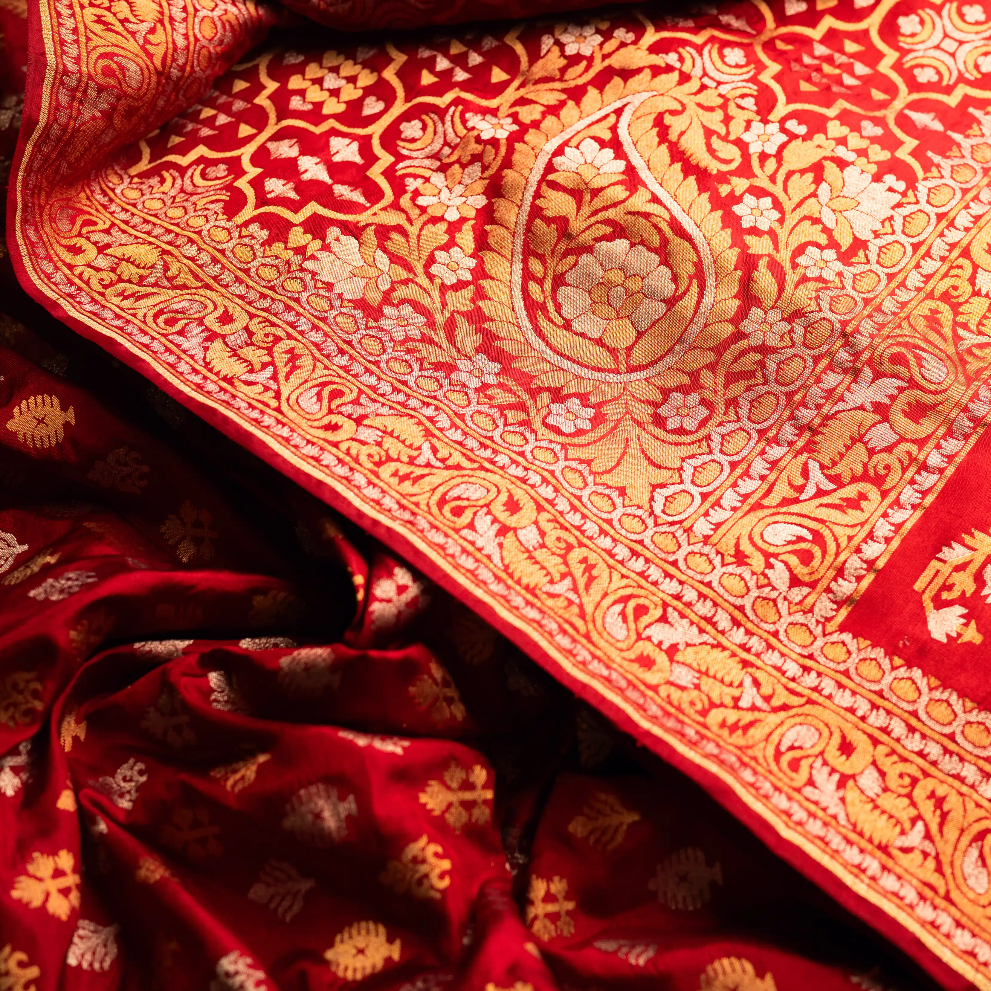 Extreme close-up of the red Nilambari Iktara silk fabric, highlighting a large handwoven gold zari paisley (kalka) motif and the intricate floral border.