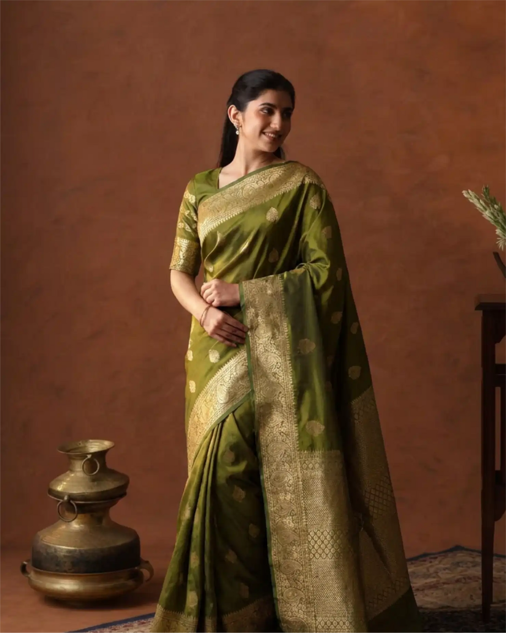 A woman wearing an elegant olive green Pure Kanjivaram silk saree with intricate gold zari weaving.