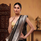A woman modeling a black handwoven Banarasi satin silk saree featuring an elegant stripe pattern and a heavy gold zari border.