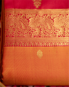 Close-up of a handwoven orange and pink Kanjivaram silk saree featuring a rich gold zari brocade border with traditional paisley patterns and a delicate buta motif on the orange body.