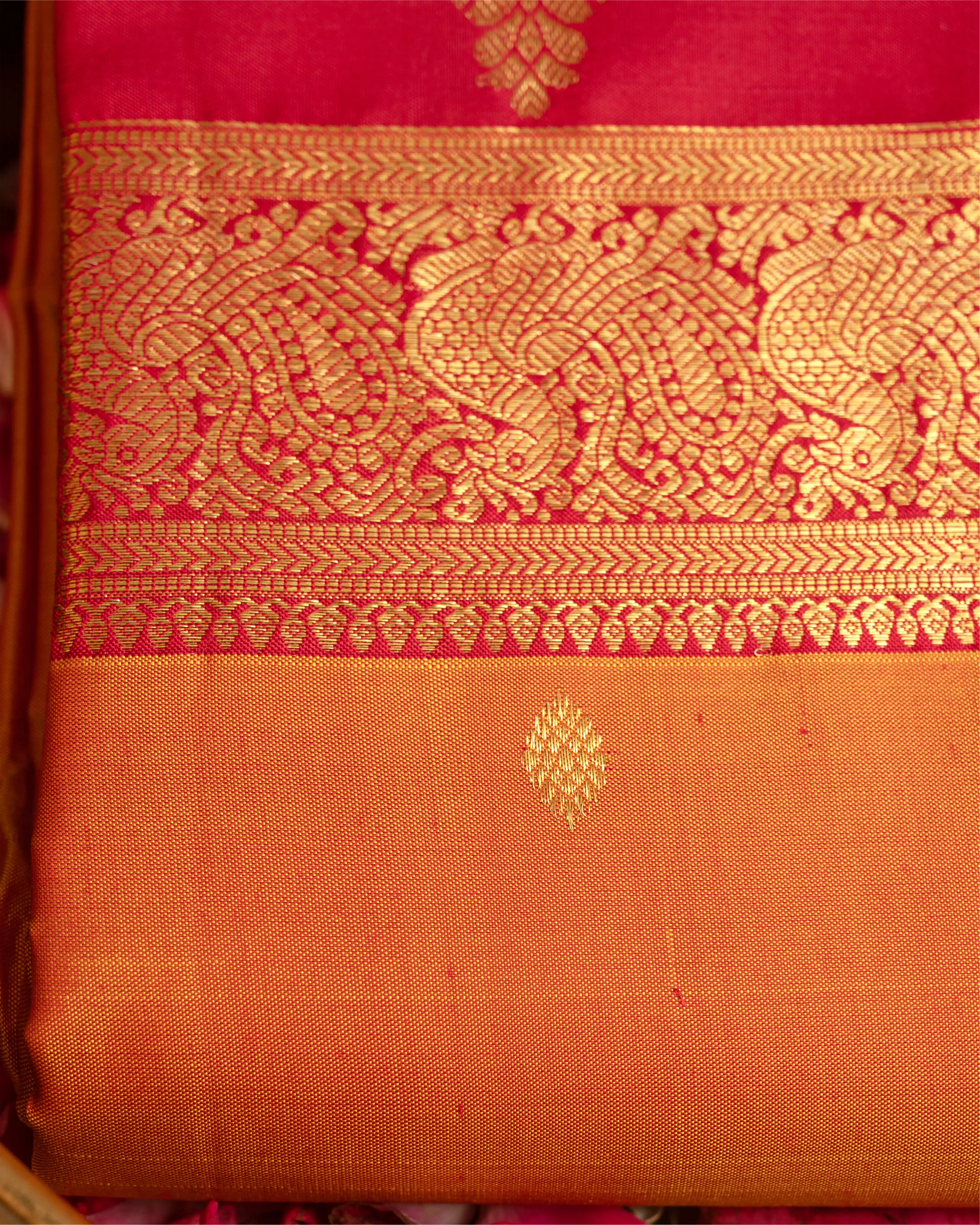 Close-up of a handwoven orange and pink Kanjivaram silk saree featuring a rich gold zari brocade border with traditional paisley patterns and a delicate buta motif on the orange body.