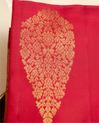 Close-up of a bright pink Kanjivaram silk saree featuring a large ornate gold brocade paisley motif and a detailed woven border along the side