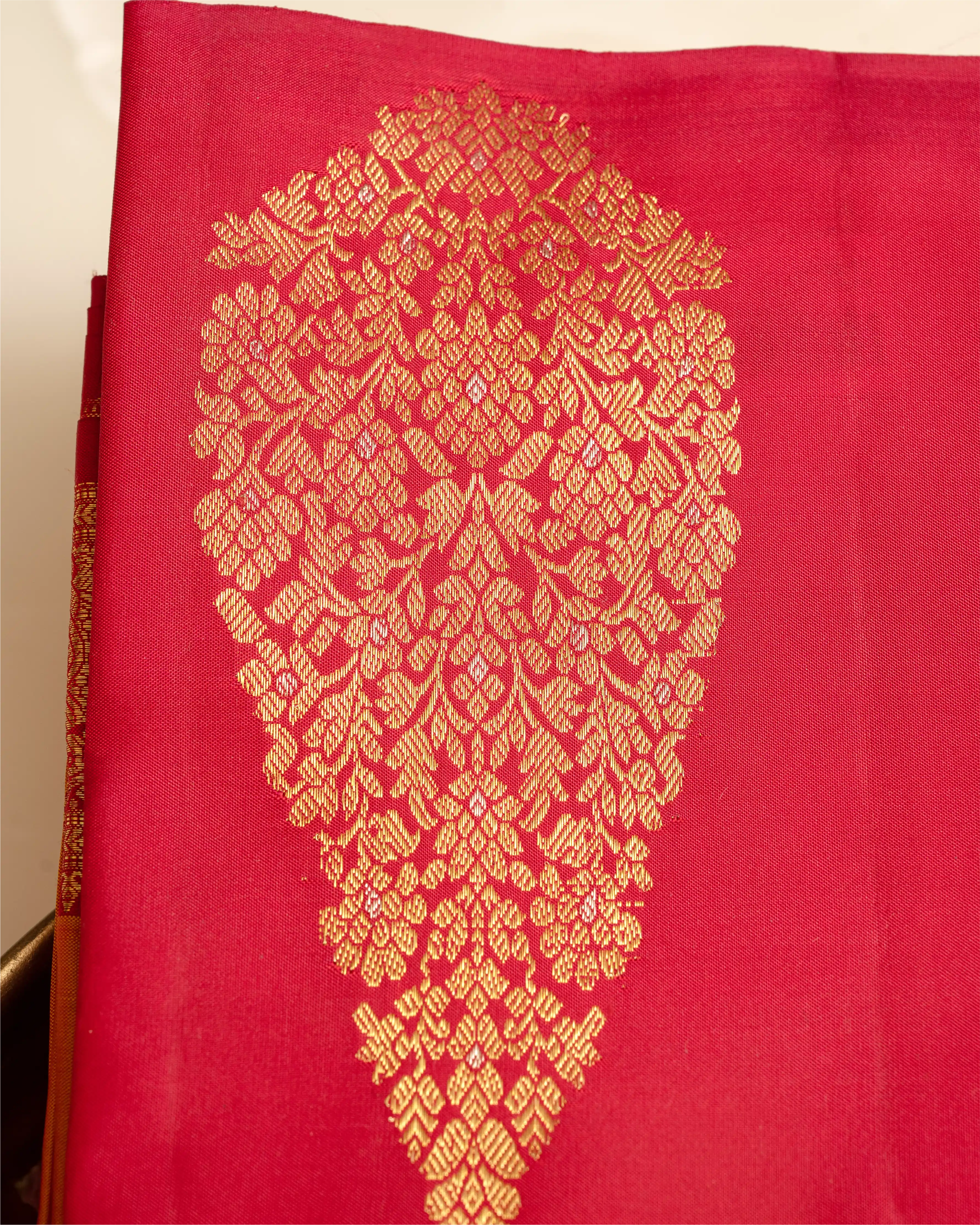 Close-up of a bright pink Kanjivaram silk saree featuring a large ornate gold brocade paisley motif and a detailed woven border along the side