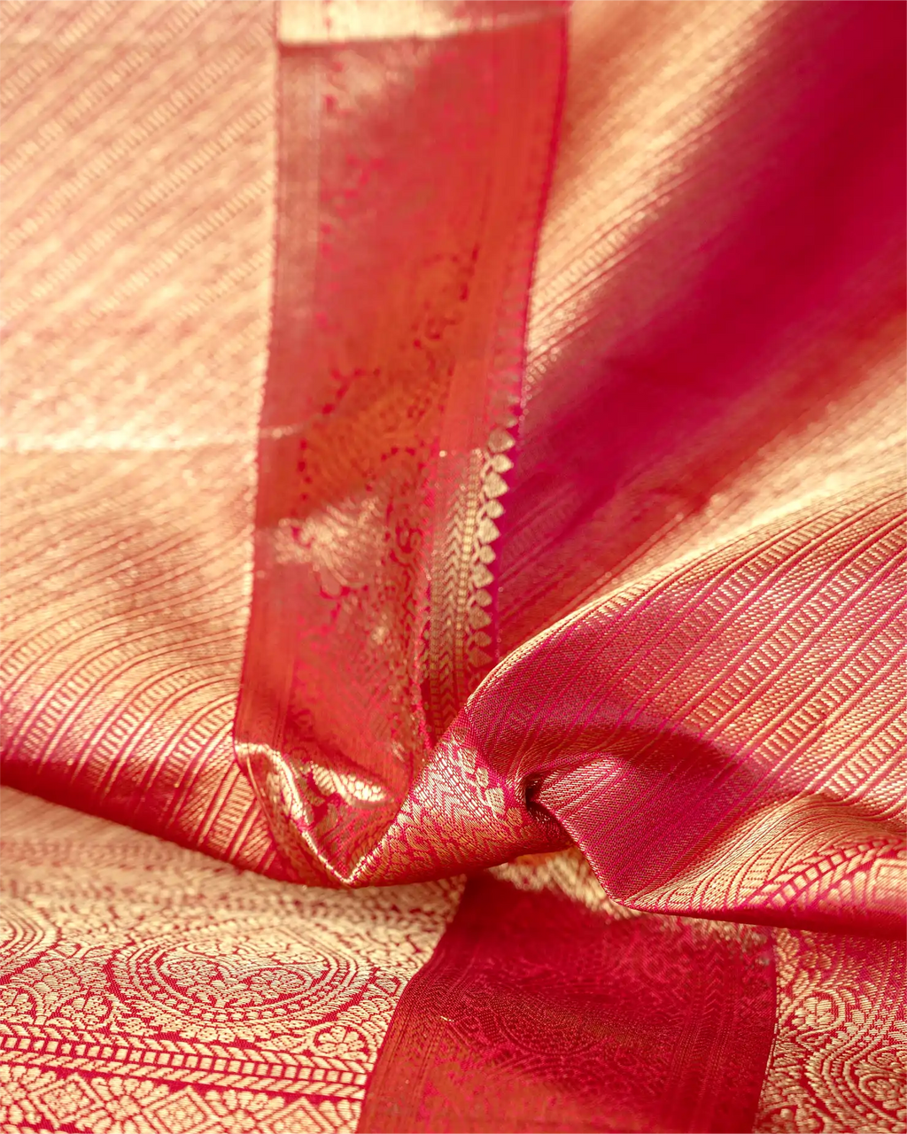 Close-up of a neatly folded orange and pink Kanjivaram silk saree highlighting the rich texture, shimmering gold zari pleats, and intricate traditional border.