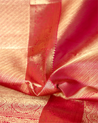 Close-up of a neatly folded orange and pink Kanjivaram silk saree highlighting the rich texture, shimmering gold zari pleats, and intricate traditional border.