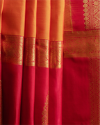 Close-up of neatly pleated orange and red Kanjivaram silk saree fabric highlighting the intricate gold zari woven borders and rich texture
