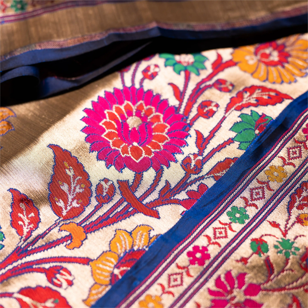 Detailed close-up of a royal blue Paithani Patola silk saree featuring a large pink and orange handwoven floral motif and a traditional zari border.