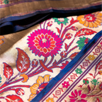 Detailed close-up of a royal blue Paithani Patola silk saree featuring a large pink and orange handwoven floral motif and a traditional zari border.
