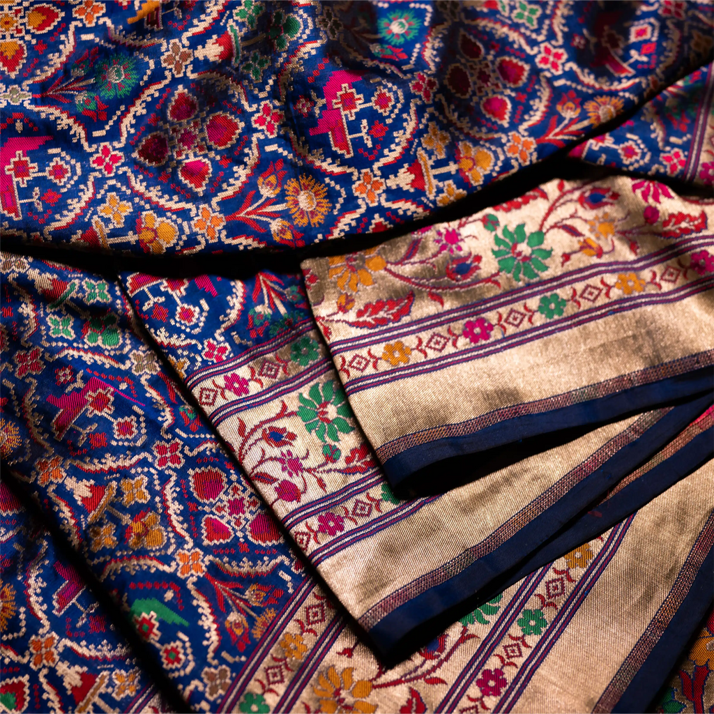 Extreme close-up of a royal blue Paithani Patola silk saree showcasing the fine handwoven gold and silver zari border with traditional floral patterns.