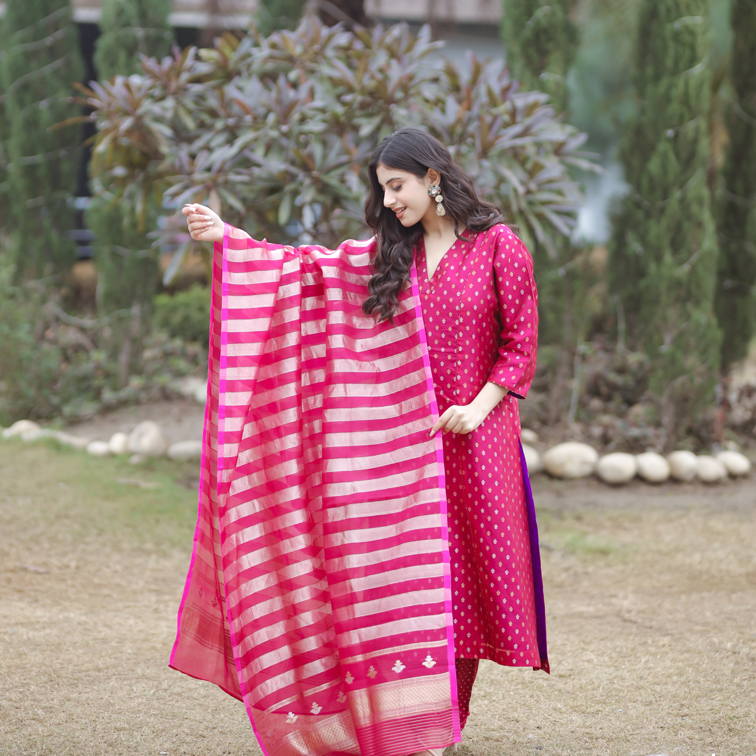 Full-view of a woman in a pink handwoven Banarasi silk suit with gold and silver Sona Rupa motifs, elegantly draping a pink and gold striped organza tissue dupatta.