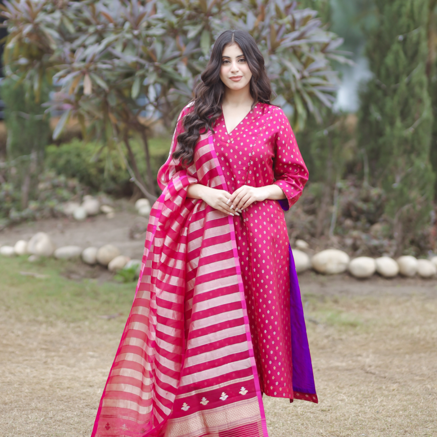 Woman wearing a pink and purple handwoven Banarasi silk suit with gold and silver Sona Rupa motifs, paired with a striped organza tissue dupatta.
