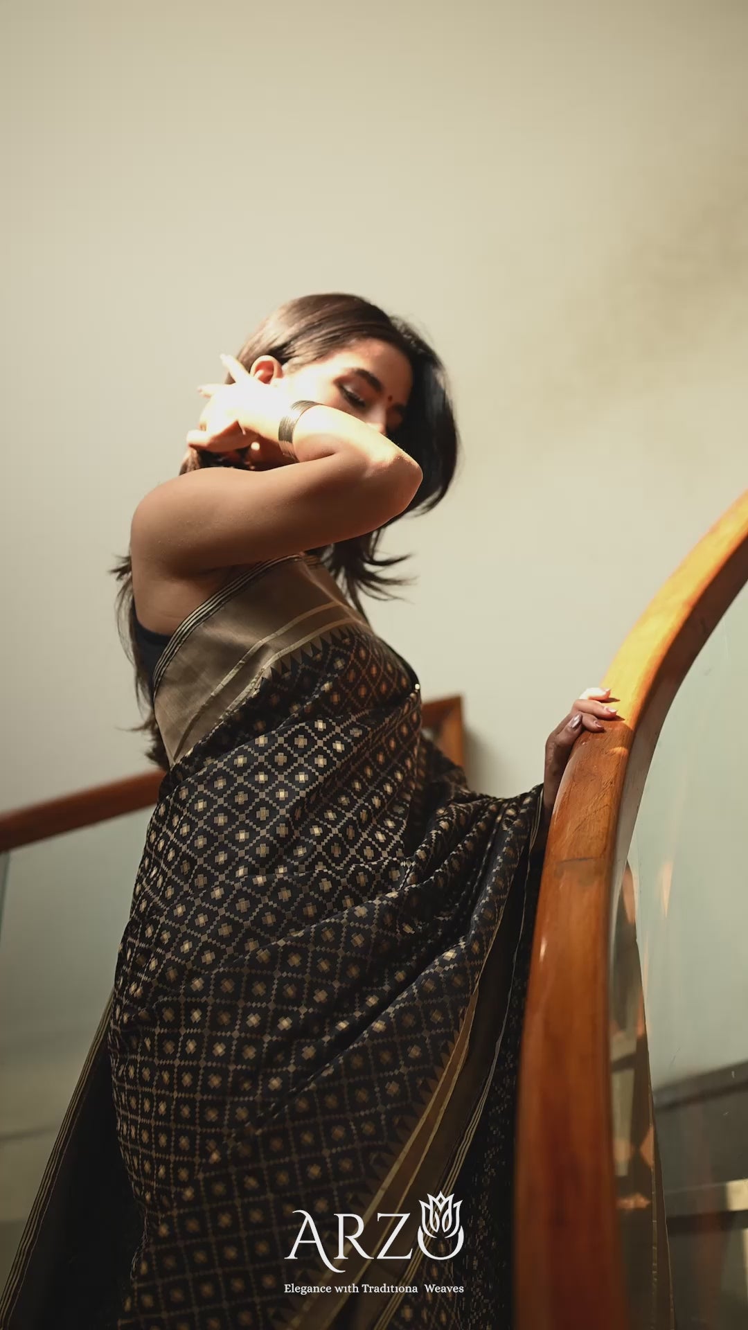 A model gracefully draped in the Black Handwoven Katan Silk Saree, highlighting the shimmering gold zari floral motifs and the fluid movement of the pure silk fabric.