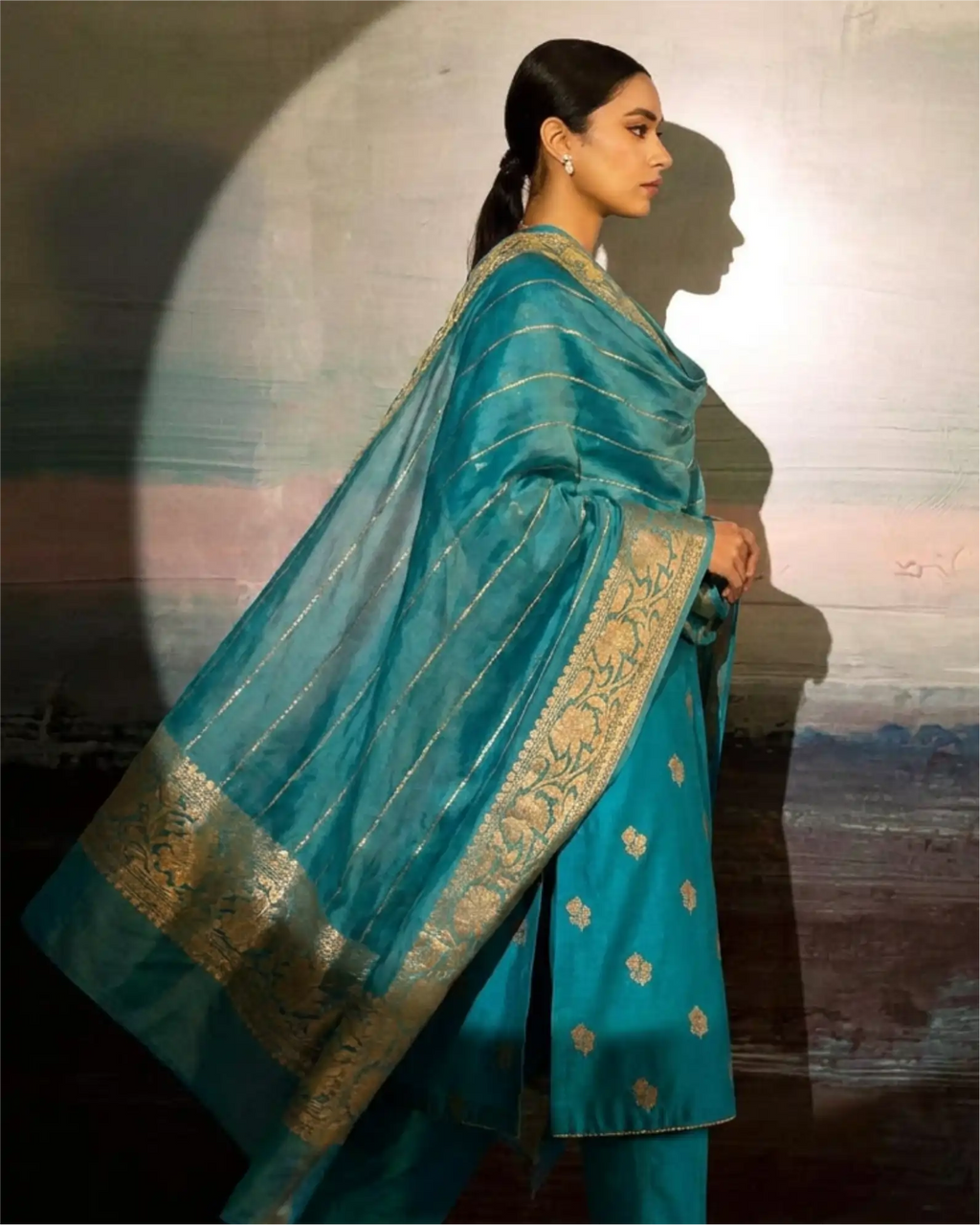 A model wearing a premium dark teal pure Banarasi silk suit with a matching Kora dupatta, featuring traditional intricate weaving.