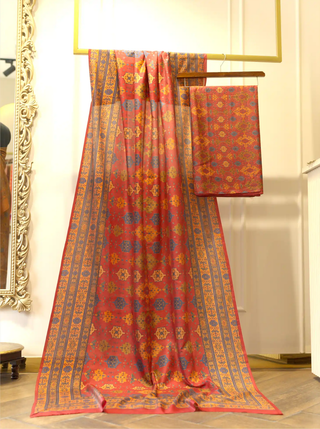 Unstitched rust red pure Boski silk suit draped on a display stand showing traditional geometric print work and ornate border with matching folded fabric