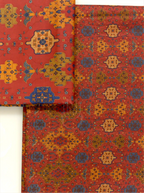 Folded rust red pure Boski silk fabric close-up showing detailed geometric and ethnic print pattern with mustard yellow and slate blue accents
