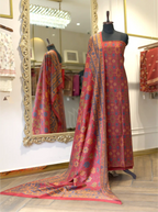 Unstitched rust red pure Boski silk suit draped on a mannequin with matching printed dupatta spread out in a boutique store setting