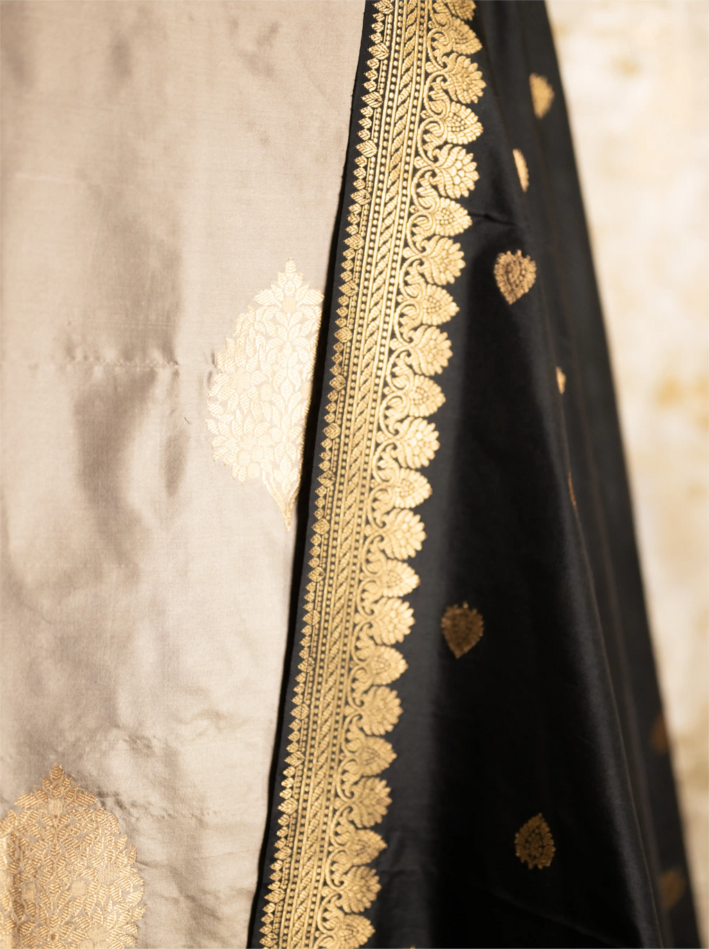 Close-up of intricate gold zari embroidery on a black Katan silk dupatta with a textured beige background.