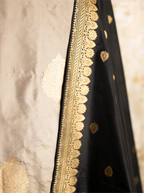 Close-up of intricate gold zari embroidery on a black Katan silk dupatta with a textured beige background.