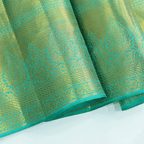 Macro shot of the pure Kanjivaram silk saree fabric, detailing the rich green and blue weave texture and authentic metallic zari craftsmanship.
