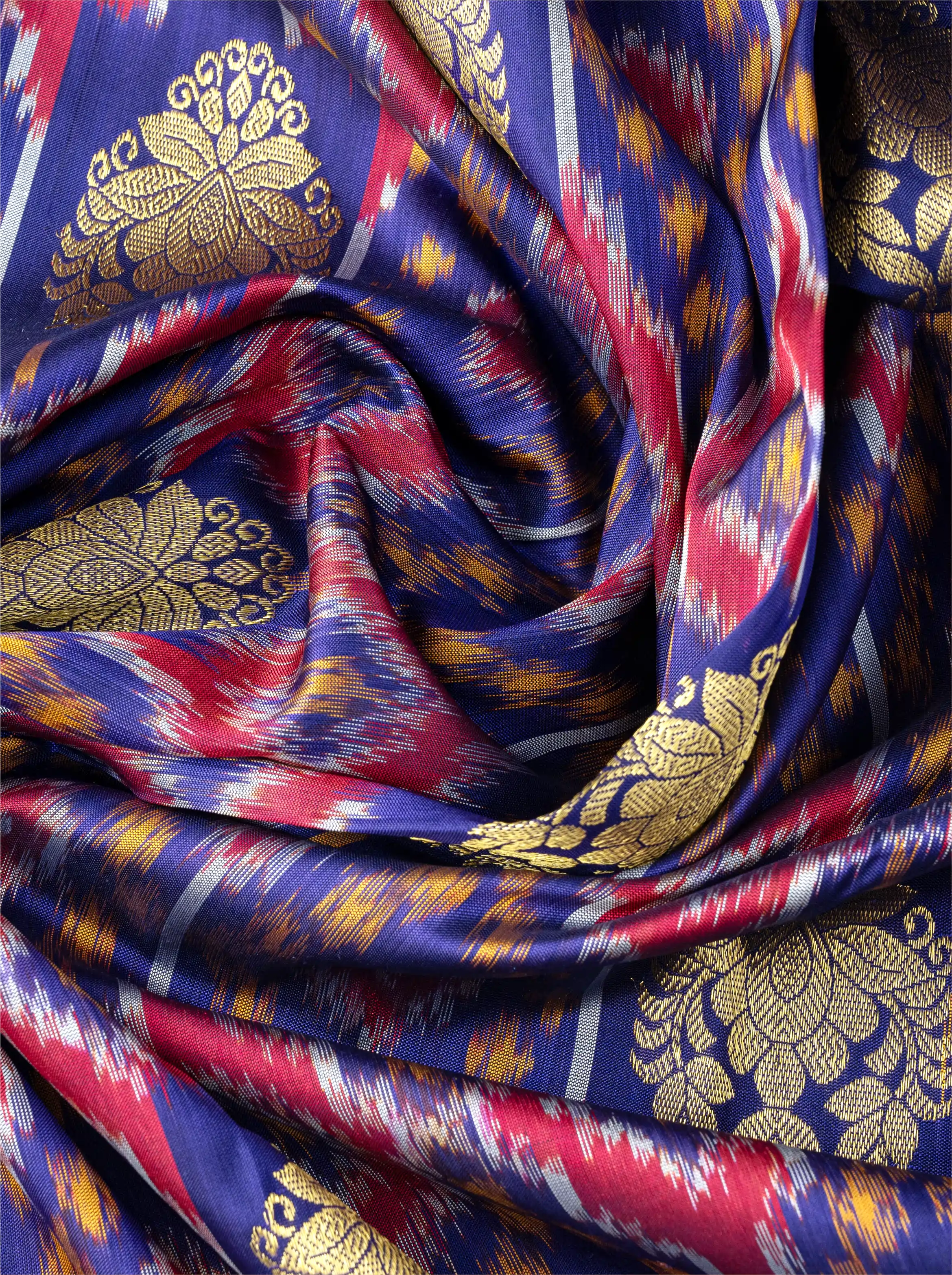Macro shot of handwoven purple Patola silk saree showing a prominent metallic gold zari floral brocade motif over colorful ikat patterns.
