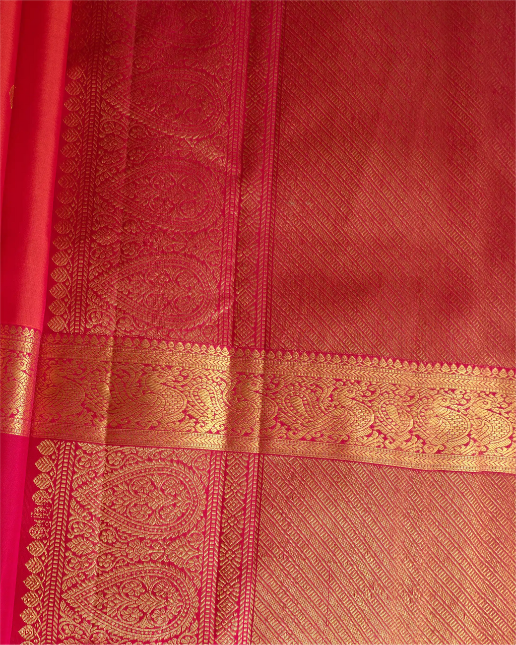 Close-up detail of a red silk saree featuring an intricate gold zari woven border and traditional paisley patterns.