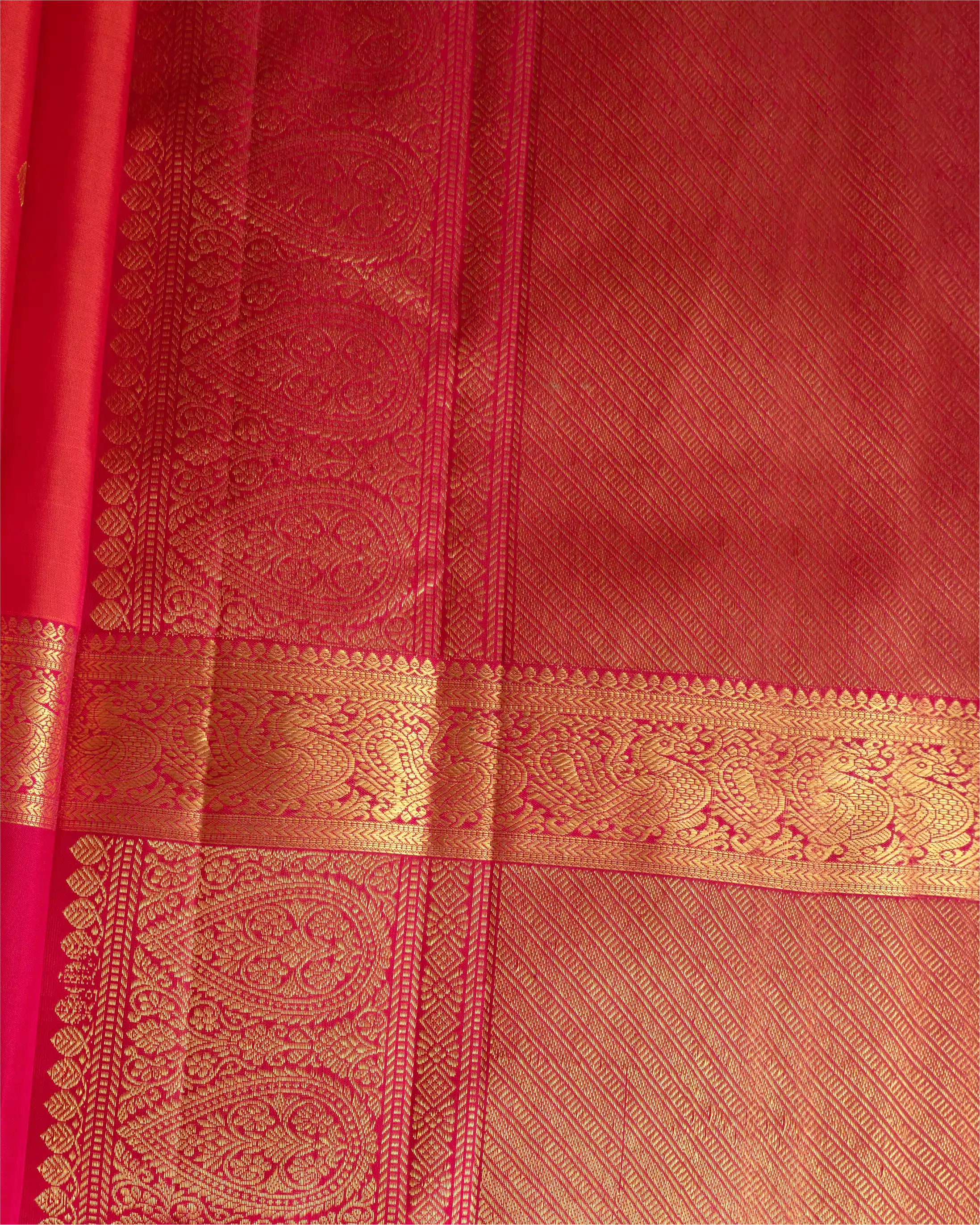Close-up detail of a red silk saree featuring an intricate gold zari woven border and traditional paisley patterns.