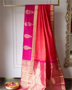 Handwoven red and pink Kanjivaram silk saree with a traditional gold zari border and buta motifs, displayed on a gold-framed hanger.
