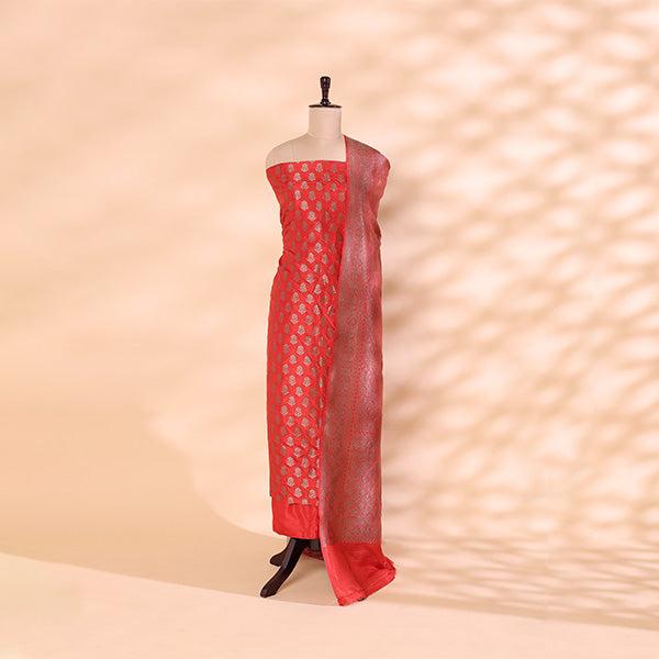 A vibrant red Banarasi silk suit featuring an intricate full Jaal handwoven design, elegantly displayed on a mannequin against a soft geometric patterned backdrop.