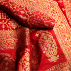 Detailed view of the red Nilambari Iktara silk fabric showing the rich texture, folded drapes, and traditional gold zari floral weaving