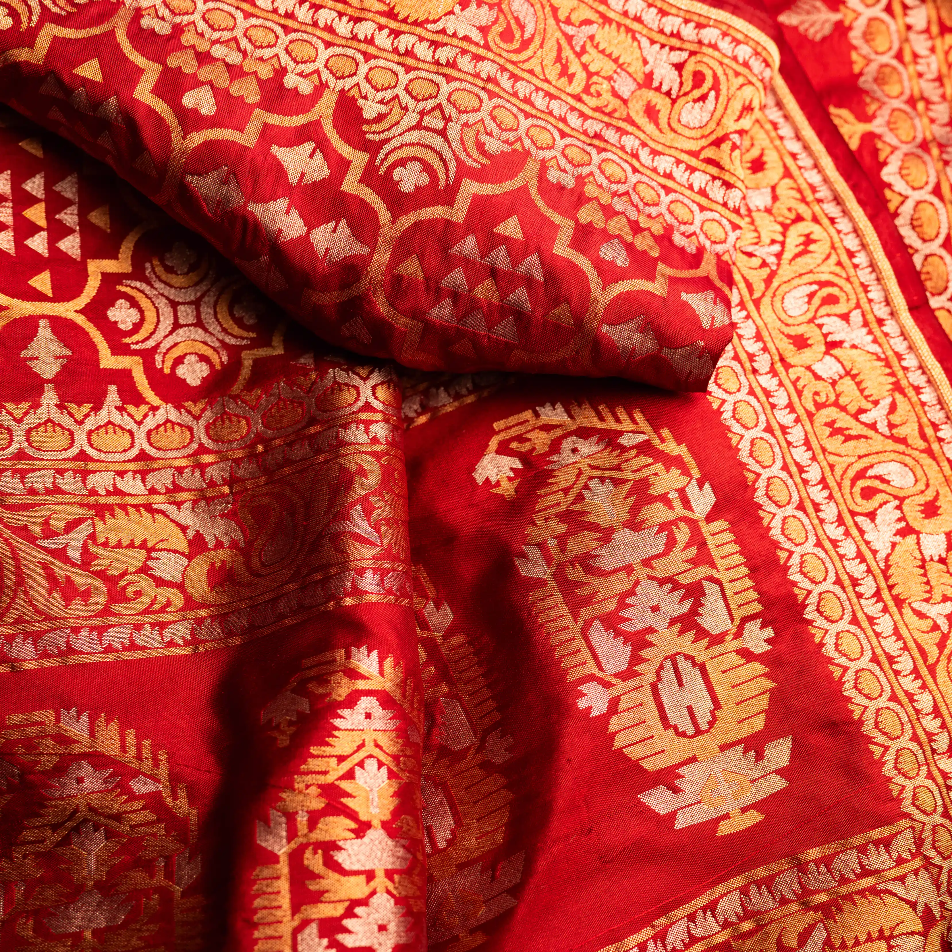 Detailed view of the red Nilambari Iktara silk fabric showing the rich texture, folded drapes, and traditional gold zari floral weaving