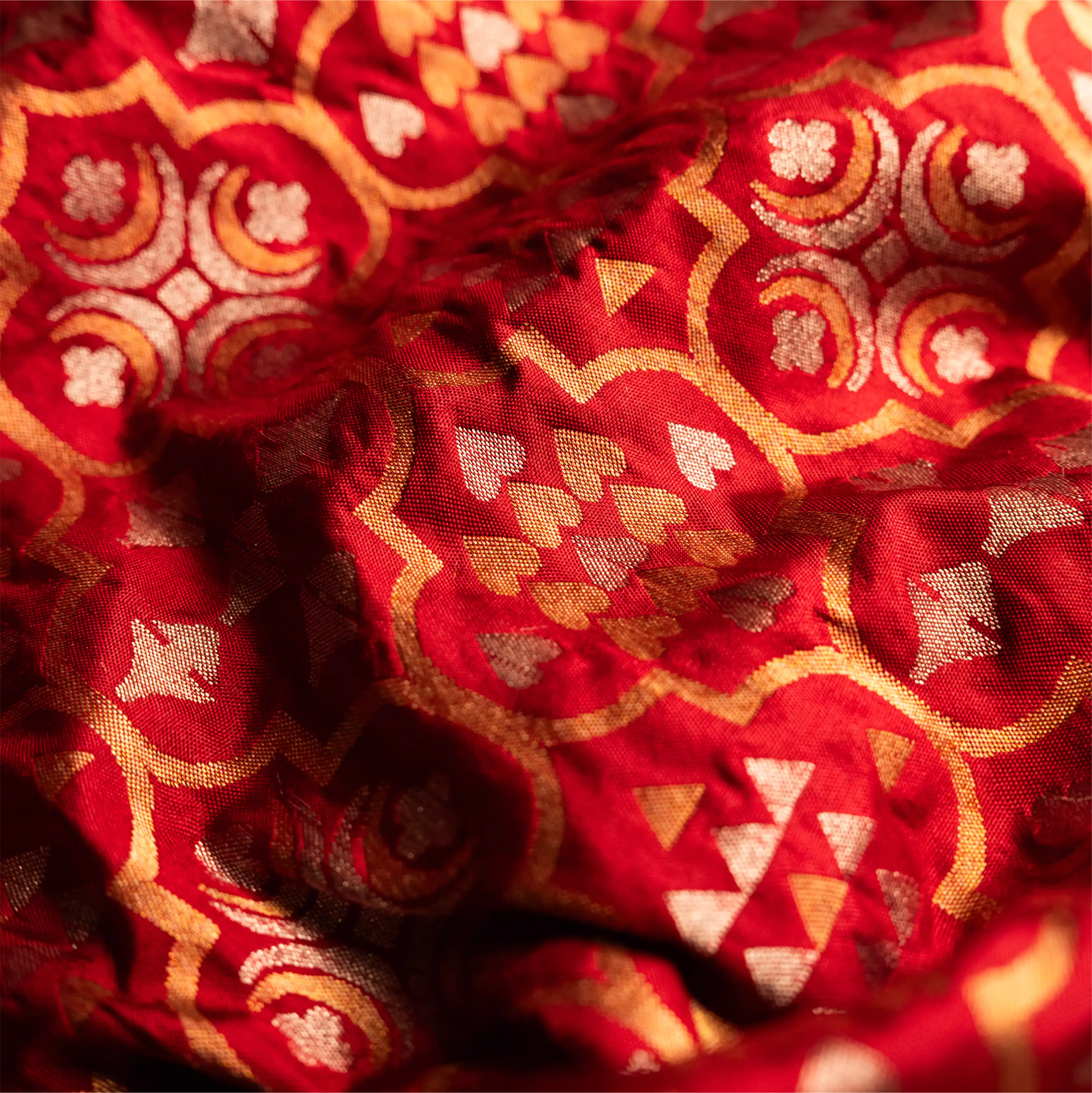 Close-up of handwoven Nilambari Iktara silk fabric featuring a mixture of gold and silver zari motifs in a traditional geometric floral pattern