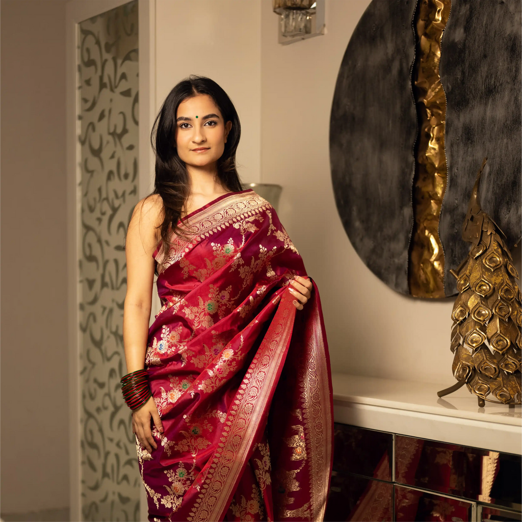 Model wearing a Red Handwoven Katan Silk Saree with gold zari floral motifs in a traditional indoor setting.