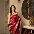 Model wearing a Red Handwoven Katan Silk Saree with gold zari floral motifs in a traditional indoor setting.