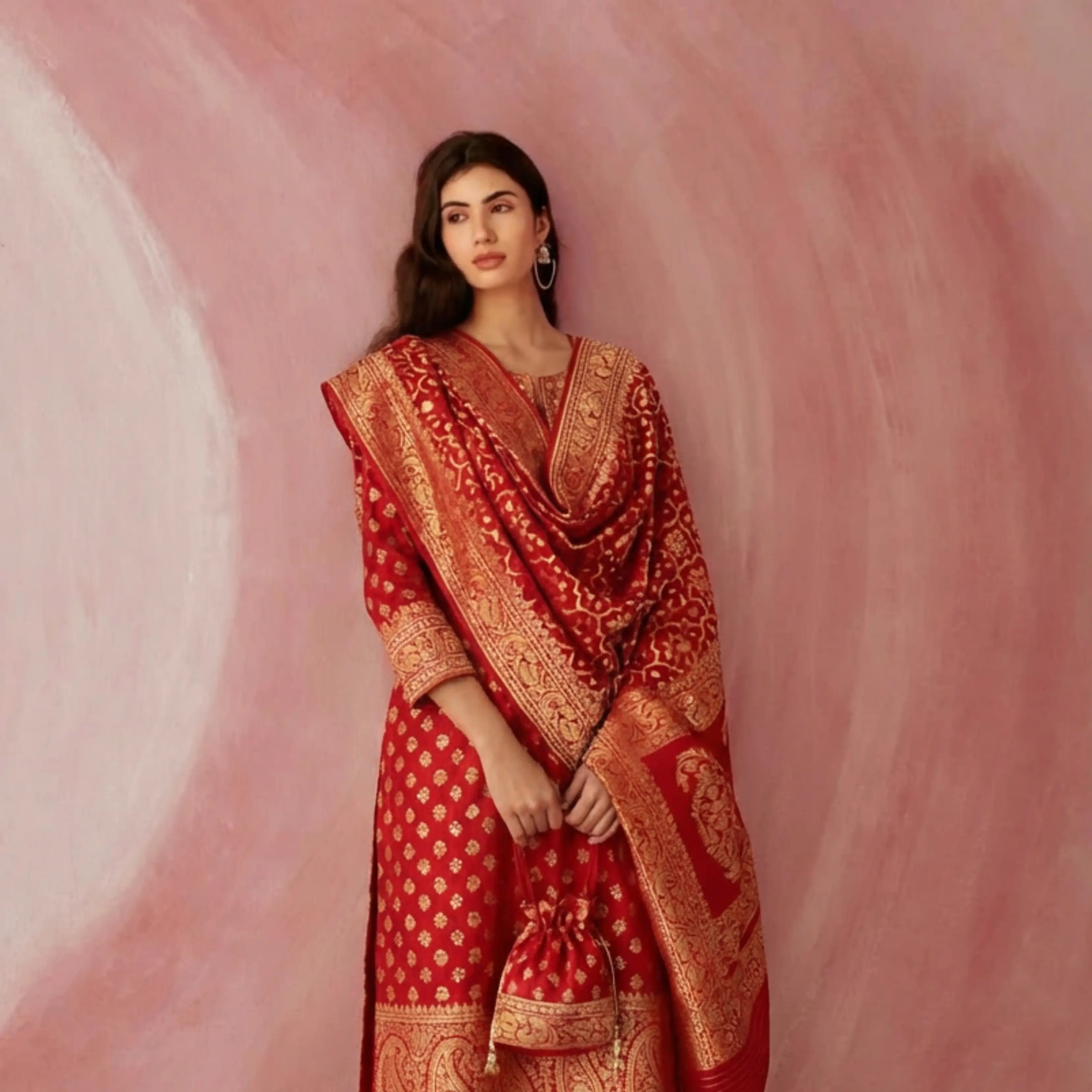 Woman wearing a crimson red Handwoven Nilambari Iktara Silk Suit with gold zari motifs, featuring a heavy matching dupatta and traditional jewelry.