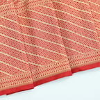 Close-up of the unstitched red silk blouse fabric featuring a heavy golden jaal border with traditional floral motifs.