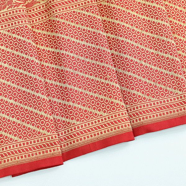Close-up of the unstitched red silk blouse fabric featuring a heavy golden jaal border with traditional floral motifs.