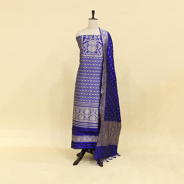 A mannequin displaying an elegant royal blue Banarasi silk suit featuring intricate silver zari work, traditional floral motifs, and a matching draped dupatta.