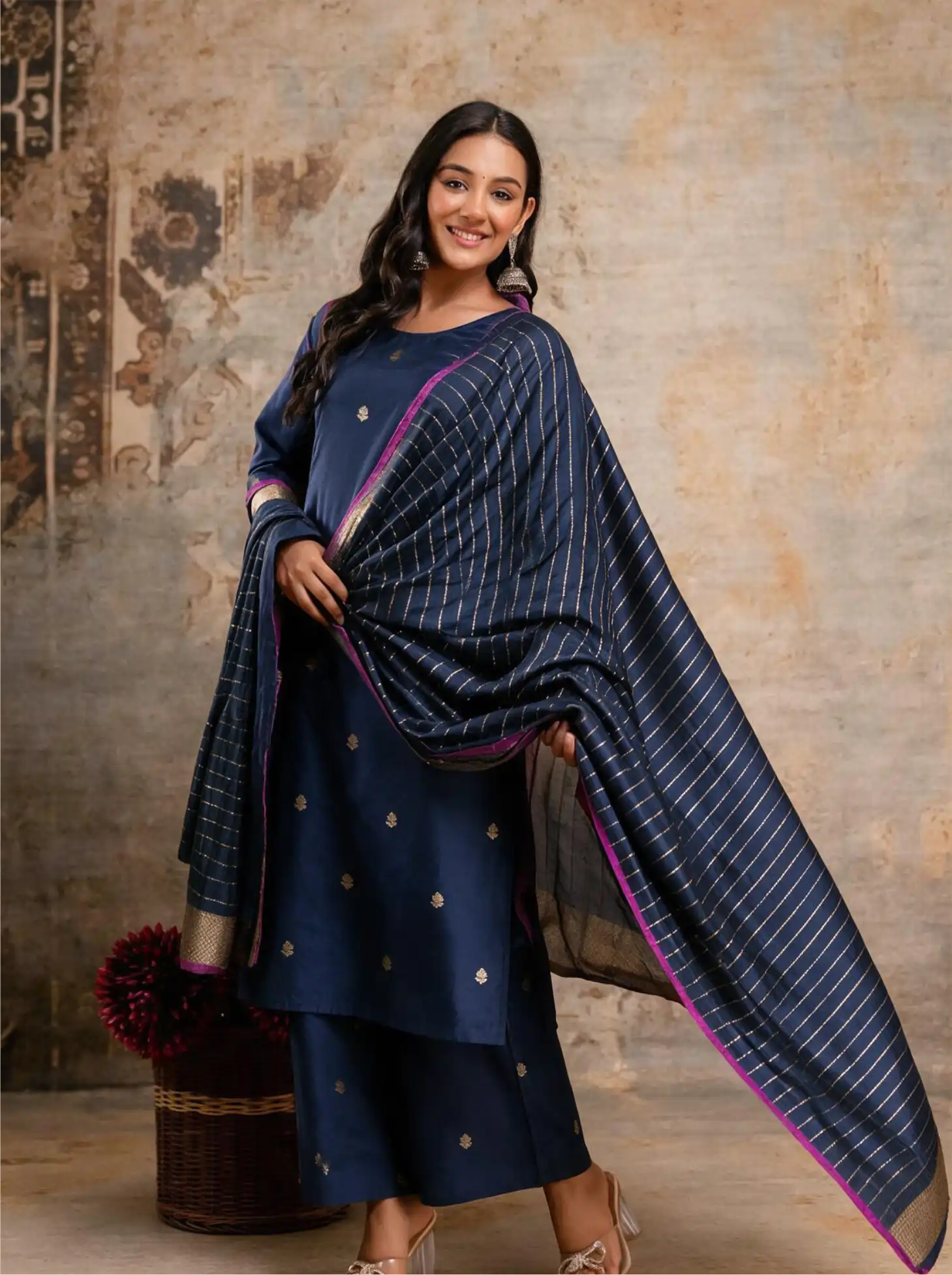 Smiling model wearing a stitched royal blue Kora Katan silk suit with silver zari floral bootis and a matching striped zari dupatta with pink edging.