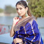 A model wearing a premium royal blue silk saree with intricate gold woven patterns, styled with elegant traditional earrings.