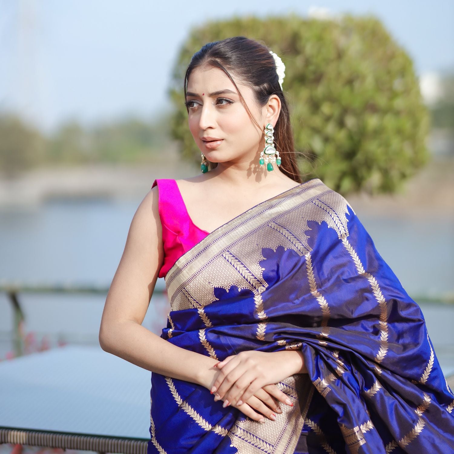A model wearing a premium royal blue silk saree with intricate gold woven patterns, paired with a vibrant pink blouse.