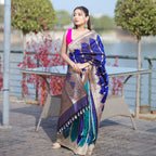 A model wearing a premium royal blue and teal silk saree with a wide gold border, paired with a vibrant pink blouse.
